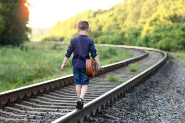 Demiryolunda gitarlı mutlu çocuk.