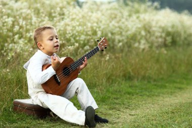 Küçük çocuk doğada gitar çalıyor.