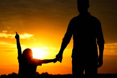 Baba ve oğulun silueti gün batımında oynuyor
