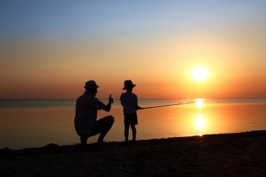 Mutlu baba ve çocuk balıkçılar deniz kenarında balık yakalar.
