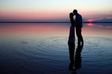 Sahilde gün batımında mutlu bir çiftin silueti.