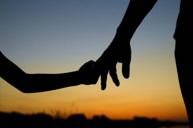 Siluet ebeveyn küçük bir çocuğun elini tutar.