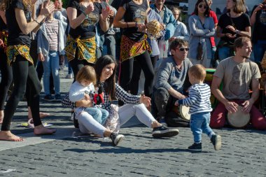 Vilnius, Litvanya, 19 Mayıs 2018: Genç Anne yere oturuyor ve halklar percusion davul müzik sokak gün oynamak için arıyorsunuz iki çocuk ile.