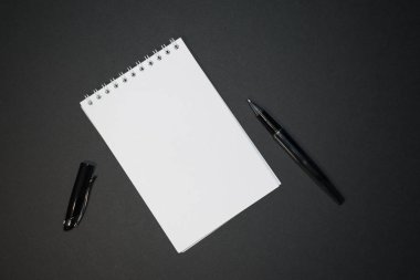 Siyah zemin üzerinde kalem olan boş bir kağıt sarmal defter. Üst yakın görünüm