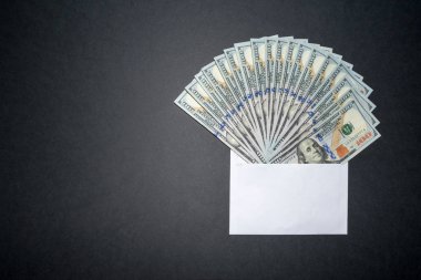 Zarfın içinde, solda kopya alanı olan karanlık bir arka plan da amerikan doları var. İçinde para olan bir zarfı paketleme. 