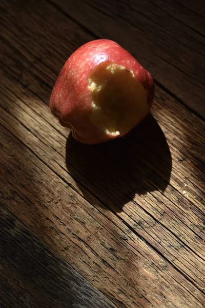 Red apple with a hole bitten into it on a brown wooden surface