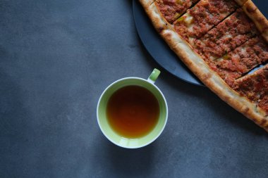Koyu arkaplanda kıymalı Türk pizzası ve bir fincan çay (kahve) 