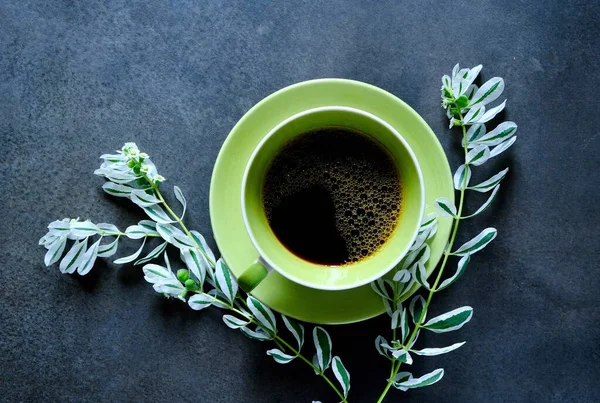 A Cup of black coffee and branch of a flower with white petals on a dark background. Coffee mood. The view from the top.