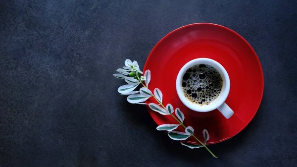 A Cup of black coffee and branch of a flower with white petals on a dark background. Coffee mood. The view from the top.