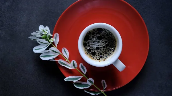 A Cup of black coffee and branch of a flower with white petals on a dark background. Coffee mood. The view from the top.