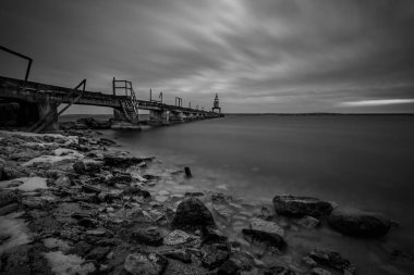 Bir iskele ile eski bir vinç ve kayaların ön planda siyah ve beyaz fotoğraf