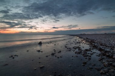 Bulutlar ve güneş battıktan sonra stoney bir plaj
