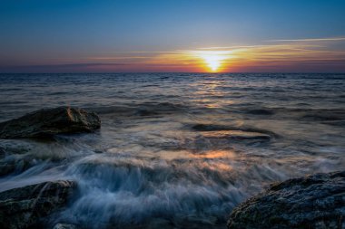 taşların üzerinde günbatımında akan dalgalar