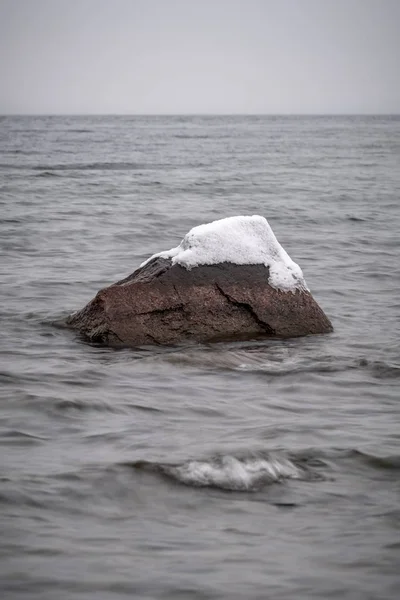 Pierre avec neige sur le dessus sortant d'un lac — Photo