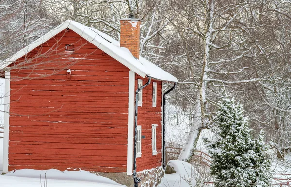 Una casa roja con nieve en el techo y bosque en el fondo — Foto de Stock