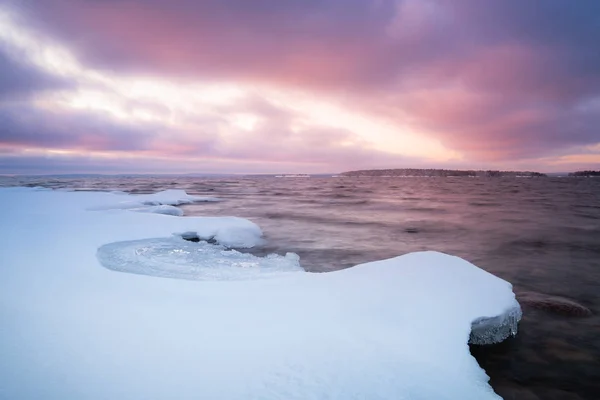 Nieve sobre rocas en la costa y puesta de sol en el fondo —  Fotos de Stock