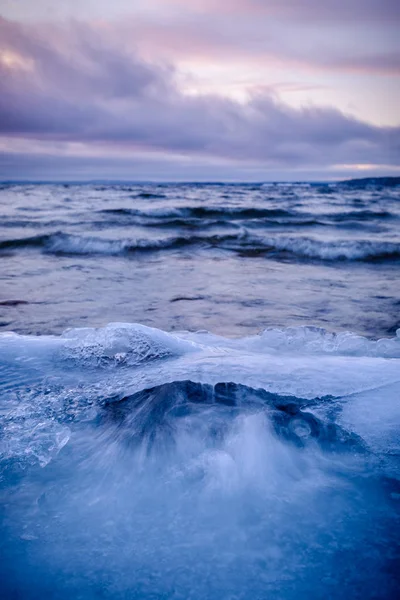 Wave flushes op een ijzige strand kleurrijke wolken op de achtergrond — Stockfoto