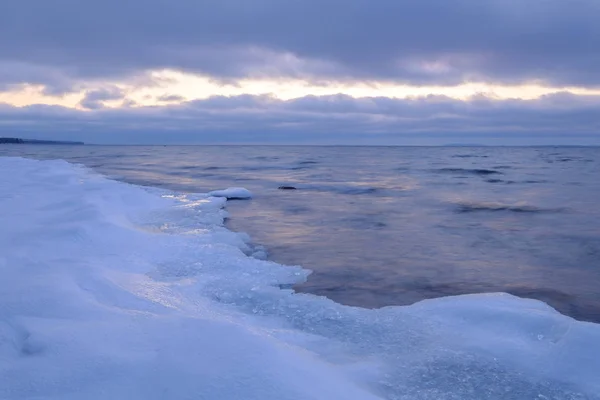 Ice and snow on a beach in the foreground, clouds and a streak o — стоковое фото
