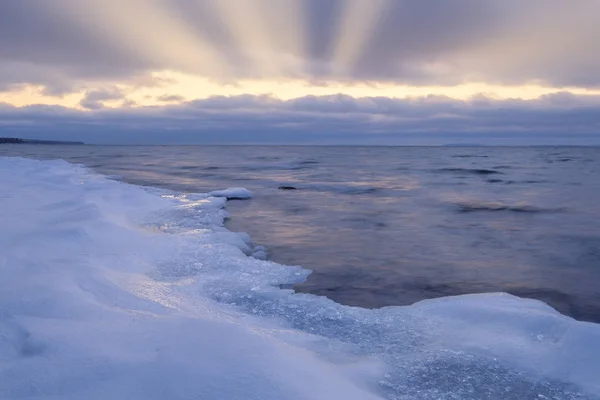 Gelo e neve em uma praia em primeiro plano, raios de sol brilhando thro — Fotografia de Stock