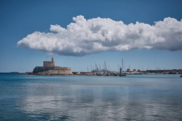 medieval castle by the sea with large white cloud over and a harbor in the background