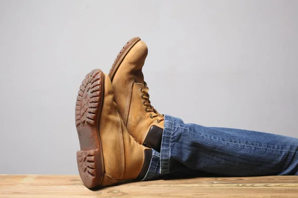lazy person concept: man\'s legs wearing  blue jeans  of desert boots rest on a wooden table with copy space for your text