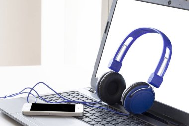 mavi kulaklık ve pc ekranında kırpma yolu ve kopyalama alanı ile bir dizüstü bilgisayarda bir akıllı telefon dinlenme