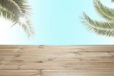 Mavi gökyüzü arkaplanı üzerinde palmiye dalları olan ahşap masa ve metin için kopyalama alanı