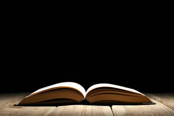 Open book on a wooden table and black background with copy space for your text