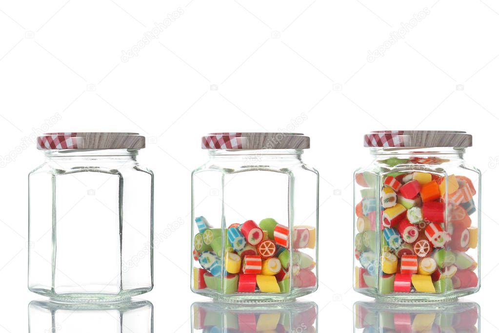 three glass jar, one empty, one half empty and one full of colored candies isolated on white background with clipping path and copy space for your text
