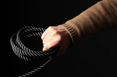 Siyah arka planda izole edilmiş siyah bir halat rulosu tutan bir adam. Metnin için kopyalama alanı var.