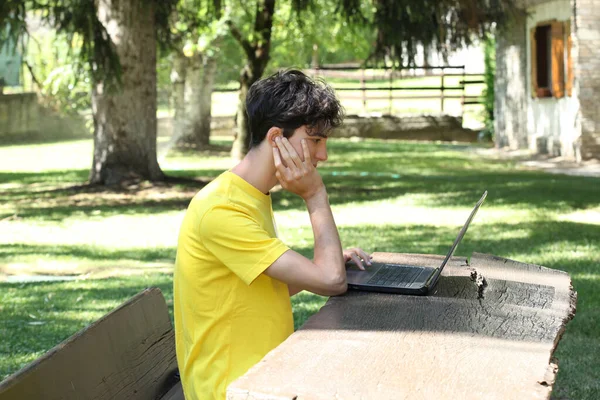 male teenager uses a computer outside in a garden with copy space for your text