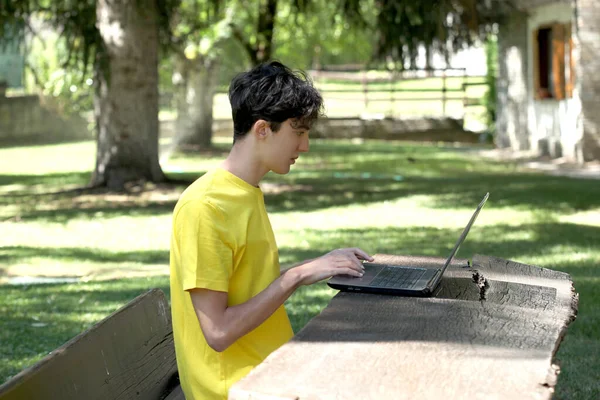 male teenager uses a computer outside in a garden with copy space for your text