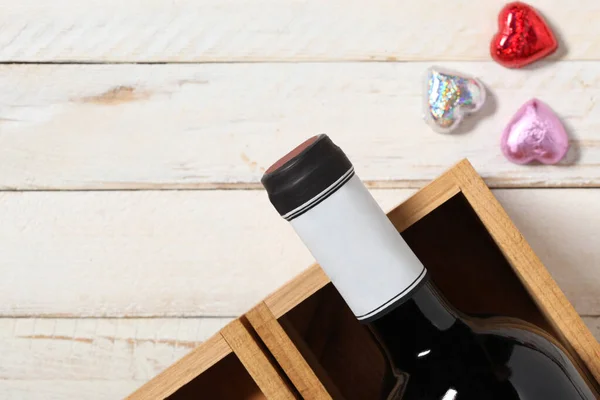 red wine bottle and hearth shape chocolate rest on a white wooden table with copy space for your text