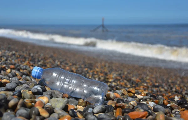 一个废弃的塑料瓶被冲刷在卵石海滩上 波浪在背景中坠毁 — 图库照片