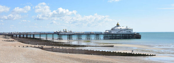 Panoramic view of the victorian Eastbourne pier in East Sussex, UK on a sunny summer day with the beach at low tide in the foreground showing the multiple groynes

