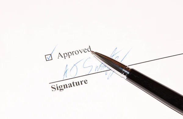 A document approval line complete with tick box and signature in blue ink and black coloured pen lying beside it.