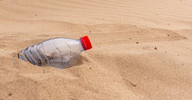 Atılan plastik su şişesi yarısı san bir plajda gömülü