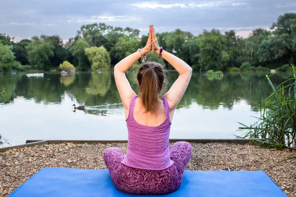 A mature yoga teacher is meditating and relaxing beside a tranquil lake by doing a yoga pose