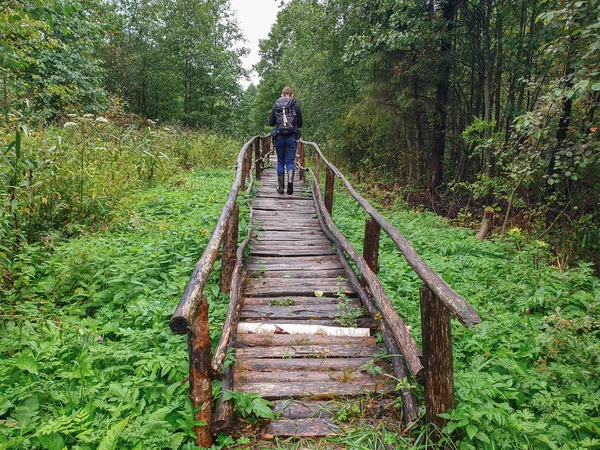 森の古い木の橋の上をリュックを持った男が歩いている。 — ストック写真