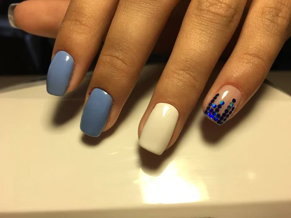 fashionable blue manicure with white design and blue pawns on a light background