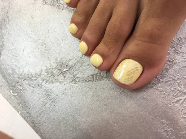 pedicure of yellow color with a fashionable design of stamping feathers