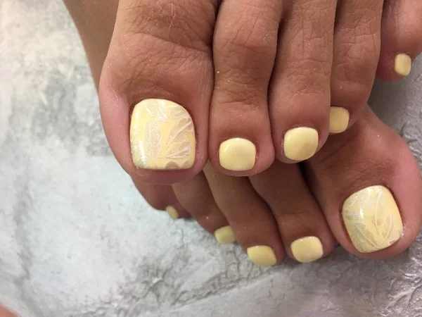 pedicure of yellow color with a fashionable design of stamping feathers