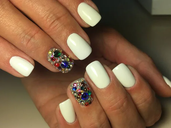 Fashionable white manicure with colored rhinestones on a textural background.