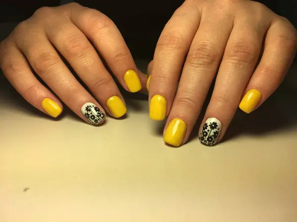 Trendy yellow manicure on a textural background with a design — Stock Photo, Image