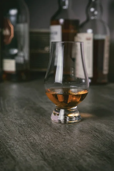 stock image Whisky glass with single malt scotch on wooden table and scotch bottles on the background