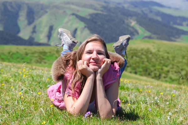 Woman tourist smiling, lying in grass against the background of summer mountains