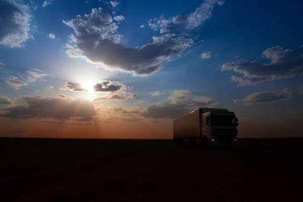 Highway. Blue with orange gradient sky with big clouds. Clouds cover the sun and droping sunrays down the earth