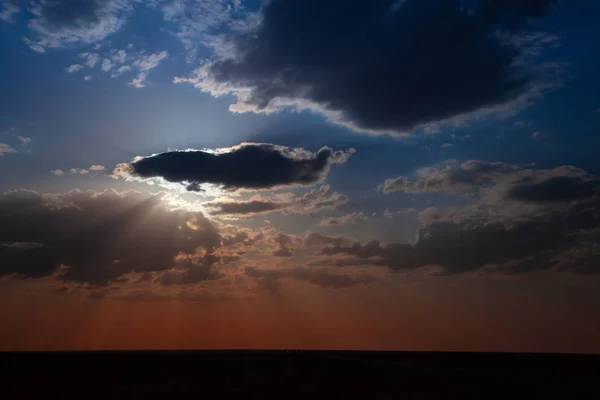 Blue sky with big clouds. Clouds cover the sun, sunlight smoothly covering the lower part of the horizon in warm colors