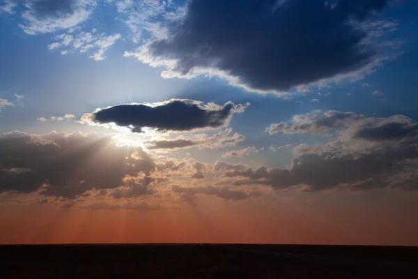 Blue sky with big clouds. Clouds cover the sun, sunlight smoothly covering the lower part of the horizon in warm colors