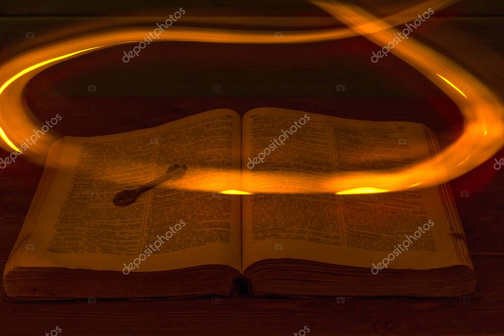 The open Holy Bible is on the table. Ancient key. A fire flying over the Bible illuminates its pages. Religion